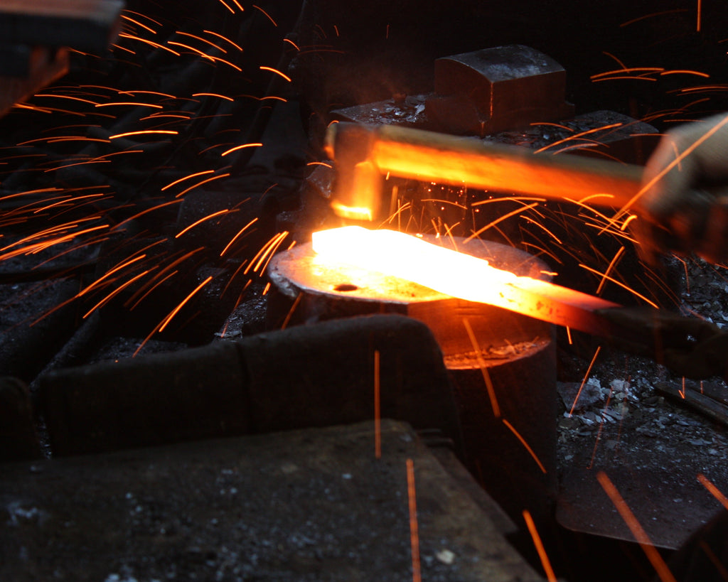 Japanese blacksmith forging a tool in a fiery forge, with sparks flying, showcasing traditional craftsmanship and skill in metalworking.