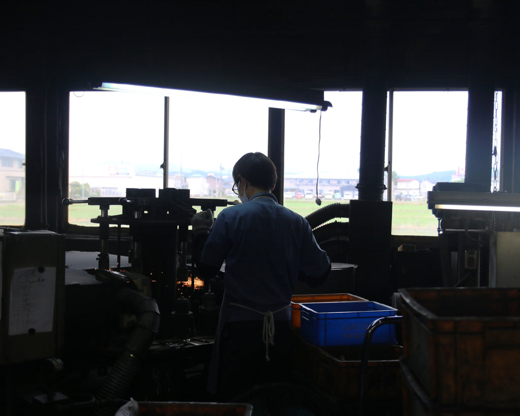 Craftsman working in a Japanese tool factory, surrounded by machinery, highlighting traditional craftsmanship in a modern workshop setting.