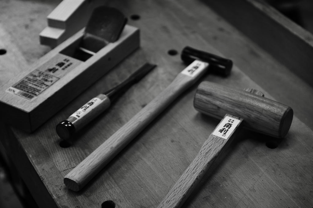 Close-up black and white image of Kakuri's traditional Japanese woodworking tools, including chisels, mallets, and a hand plane, showcasing their precision and craftsmanship.